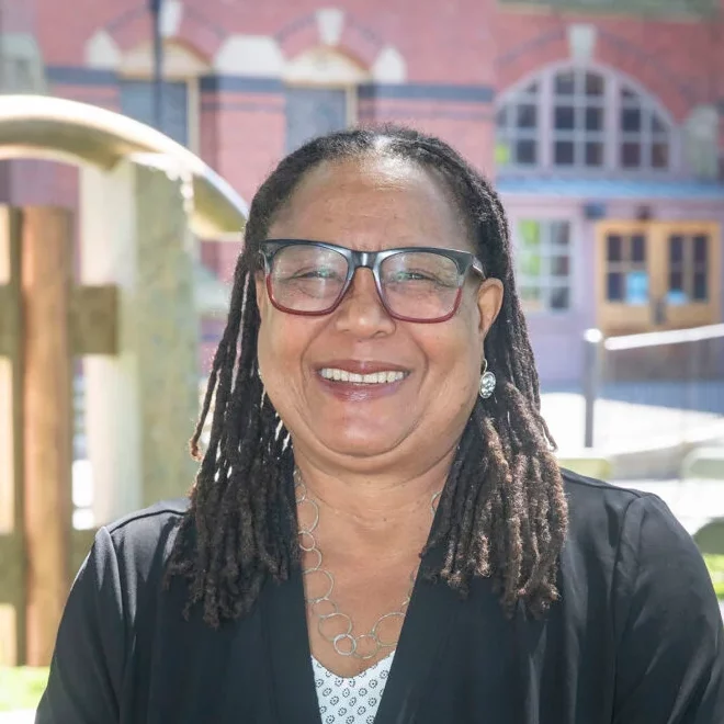 smiling woman adorned with dreadlocks and glasses.